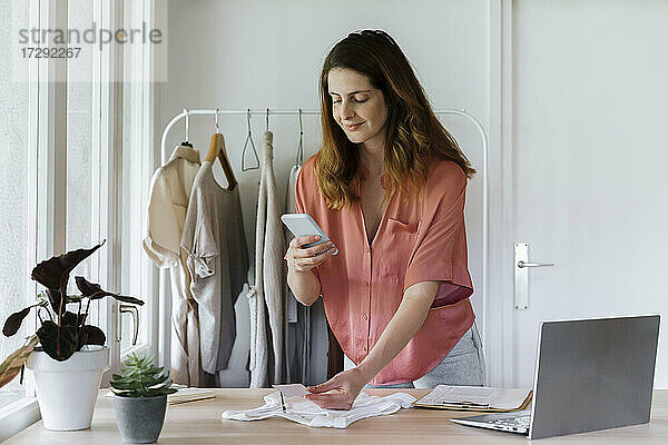 Lächelnde Geschäftsfrau  die ein Foto des Preisschildes mit ihrem Smartphone zu Hause macht