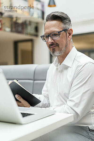 Lächelnder Geschäftsmann mit Laptop  der auf einen Laptop im Büro schaut