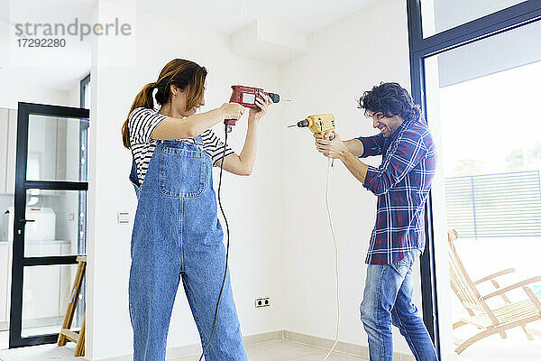 Mid adult couple playing with drill machine in new home