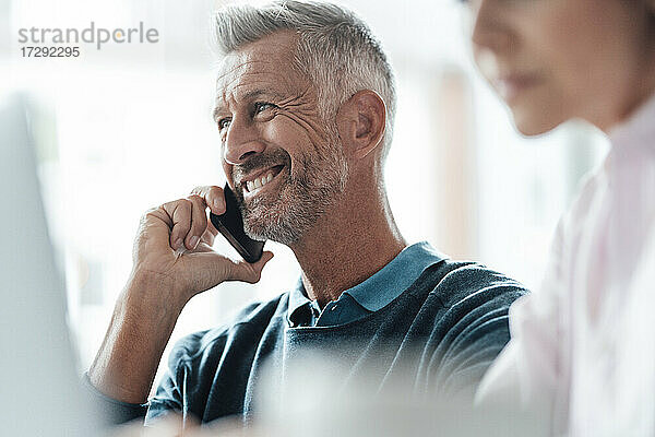 Lächelnder Geschäftsmann  der mit einem Kollegen in einem Café über sein Mobiltelefon spricht