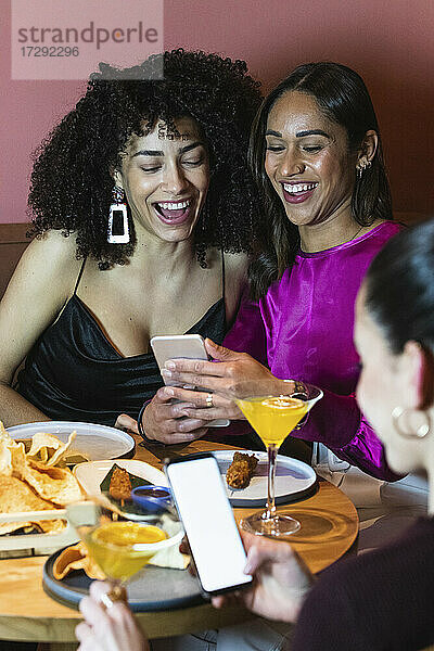 Freundinnen lächelnd bei der Benutzung von Handys am Esstisch
