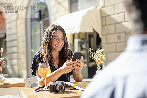 Lächelnde Frau  die ein Mobiltelefon benutzt  während sie in einem Straßencafé sitzt