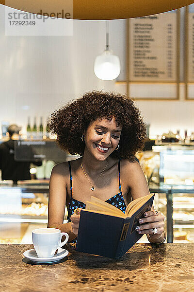 Lächelnde Frau  die in einem Café ein Buch liest