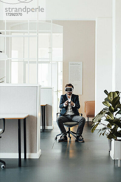 Geschäftsmann mit Virtual-Reality-Headset hält Videospiel-Controller im Büro