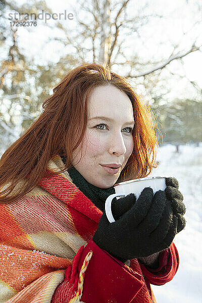 Rothaarige Frau hält Kaffee in der Hand und schaut im Winter weg