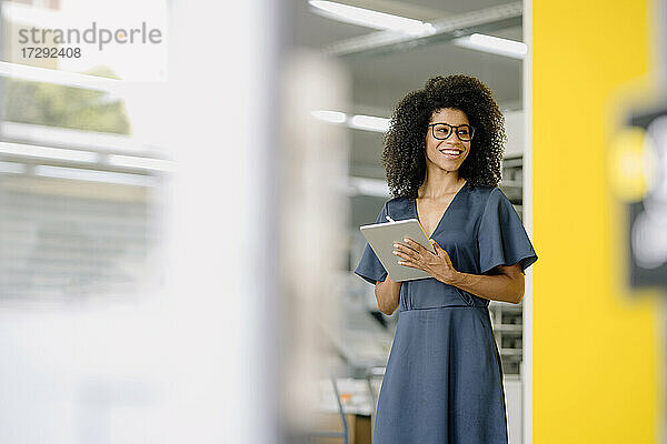 Lächelnde Geschäftsfrau  die wegschaut und ein digitales Tablet im Büro hält