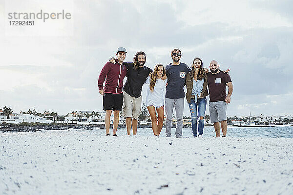 Glückliche Freunde stehen mit Arm um zusammen am Strand