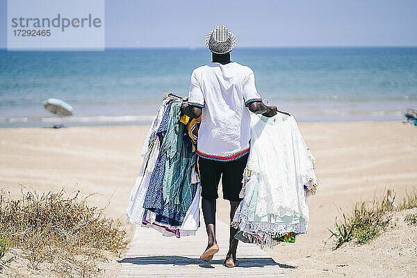 Verkäufer mit Kleidern zu verkaufen zu Fuß auf der Promenade am Strand