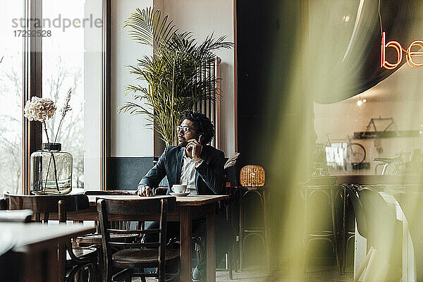 Männlicher Berufstätiger  der in einem Café sitzend mit seinem Smartphone telefoniert