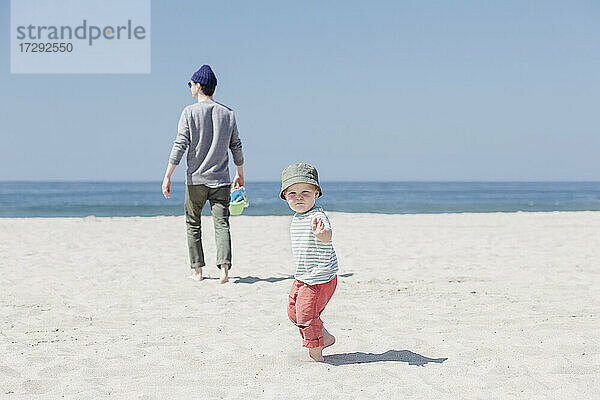 Kleiner Junge spielt  während sein Vater am Strand spazieren geht