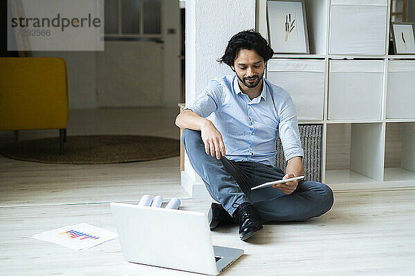 Junger männlicher Unternehmer mit Laptop und digitalem Tablet im Büro