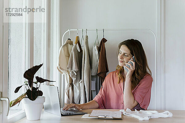 Geschäftsfrau  die einen Laptop benutzt  während sie zu Hause mit dem Handy telefoniert
