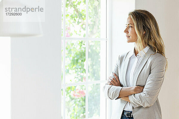 Unternehmerin schaut durch das Fenster  während sie im Büro steht