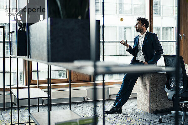Männlicher Unternehmer gestikuliert  während er im Büro am Schreibtisch sitzt