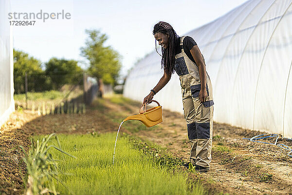 Bäuerin bewässert Pflanzen im Stehen auf einem Biohof