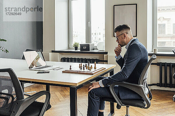 Mittlerer erwachsener Geschäftsmann lernt Schach online über Laptop im Büro
