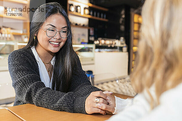 Weibliche Freunde halten sich an den Händen  während sie in einer Bar sitzen