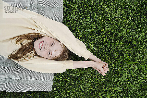 Glückliches Mädchen liegt auf einer Matte im Gras in einem öffentlichen Park