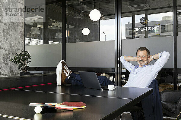 Männlicher Profi mit Händen hinter dem Kopf  der sich an einer Tischtennisplatte im Büro entspannt