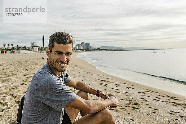 Sportler lächelnd am Strand sitzend
