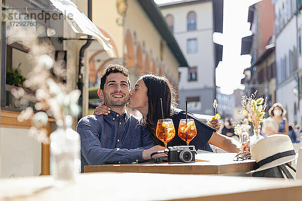 Junge Frau küsst Mann in einem Straßencafé an einem sonnigen Tag