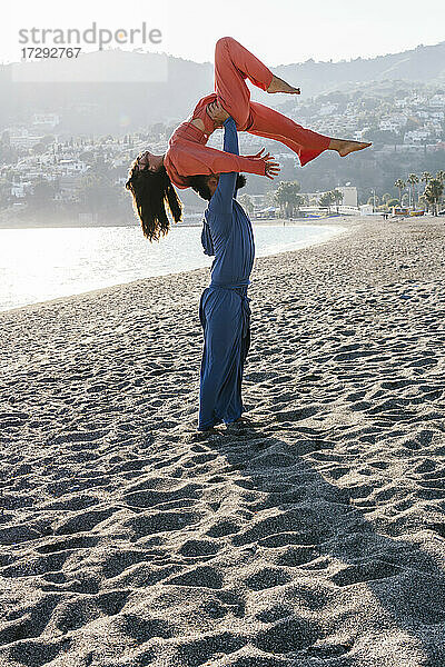 Mann trägt Frau bei Acroyoga-Übungen am Strand