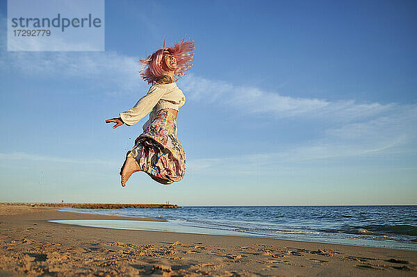 Unbekümmerte Frau  die bei Sonnenuntergang am Strand springt