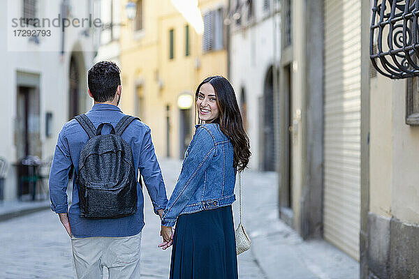 Lächelnde Frau schaut über die Schulter  während sie mit einem Mann auf der Straße spazieren geht