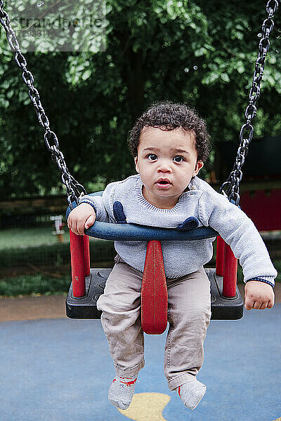 Niedlicher kleiner Junge schwingt auf einer Schaukel auf einem Spielplatz im Park