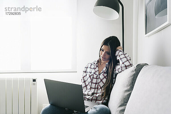 Frau benutzt Laptop  während sie zu Hause auf dem Sofa sitzt