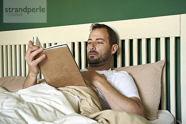 Mittlerer erwachsener Mann liest Buch im Bett zu Hause