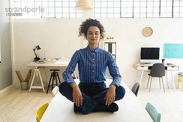 Geschäftsfrau übt Yoga im Schneidersitz auf dem Schreibtisch im Büro