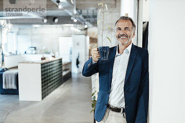Männlicher Unternehmer mit Kaffeetasse  der sich an die Wand lehnt