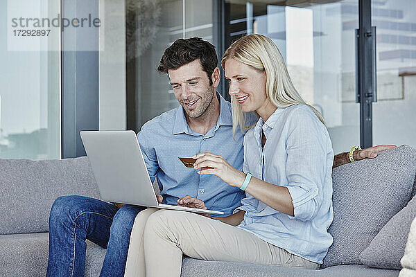 Lächelndes Paar mit Laptop beim Online-Shopping im Wohnzimmer zu Hause