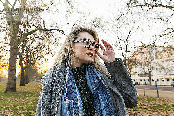 Schöne blonde Frau mit Brille steht im Park