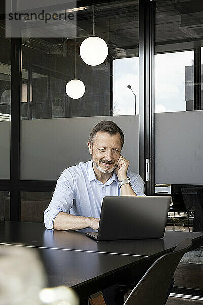 Lächelnder Geschäftsmann arbeitet am Laptop am Schreibtisch im Büro