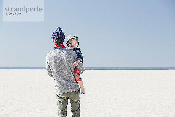 Mann  der seinen Sohn am Strand trägt  während er an einem sonnigen Tag steht