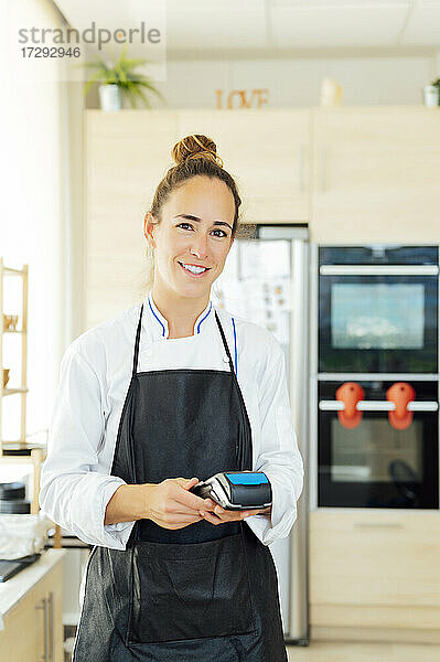 Lächelnde Köchin mit Kreditkartenleser im Restaurant