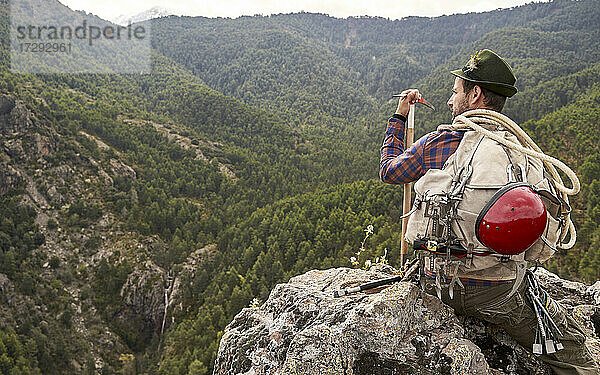 Mittlerer erwachsener männlicher Bergsteiger mit Ausrüstung auf einem Berg sitzend