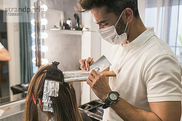 Männlicher Fachmann beim Abdecken der Haare einer Kundin mit Folie im Salon während COVID-19