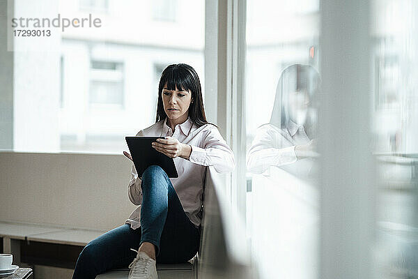 Weiblicher Besitzer  der ein digitales Tablet benutzt  während er am Fenster eines Cafés sitzt