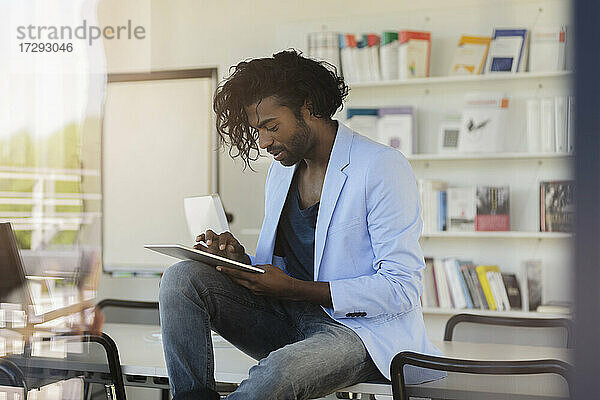 Junger Geschäftsmann  der ein digitales Tablet benutzt  während er auf dem Schreibtisch im Büro sitzt