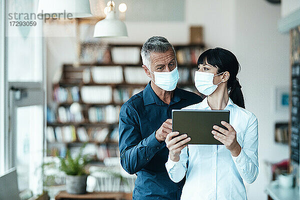 Männliche und weibliche Besitzer mit Gesichtsmaske bei der Nutzung eines digitalen Tablets in einem Café