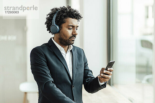 Männlicher Unternehmer  der ein Smartphone benutzt und über Kopfhörer im Büro Musik hört