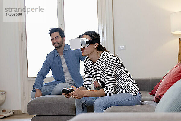 Junge Frau spielt mit Virtual-Reality-Simulator bei ihrem Freund zu Hause