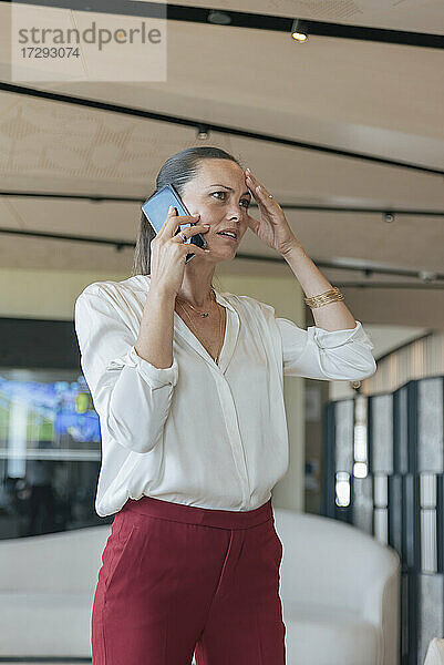 Besorgte weibliche Berufstätige  die in der Lobby mit ihrem Handy telefonieren