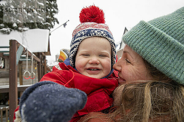 Lächelnde Frau sieht ihren fröhlichen Sohn an  während sie im Winter im Hinterhof steht