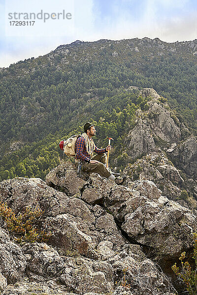 Männlicher Bergsteiger  der die Aussicht betrachtet  während er auf einem Berg sitzt