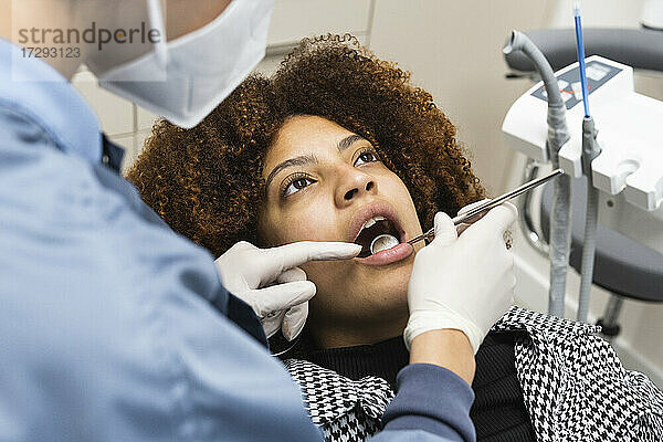 Weibliche Patientin blickt auf  während sie vom Zahnarzt während der Pandemie in der Klinik behandelt wird