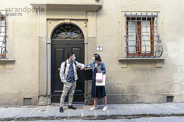 Touristenpaar mit Einkaufstüten und Gesichtsmaske grüßt durch Ellenbogenstoß auf Gehweg